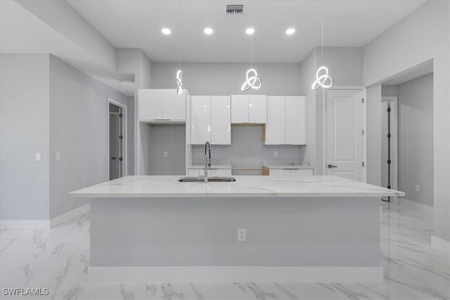 kitchen featuring pendant lighting, white cabinets, a center island with sink, sink, and light stone counters