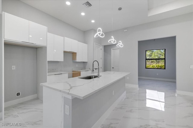 kitchen with white cabinetry, sink, hanging light fixtures, light stone counters, and a center island with sink