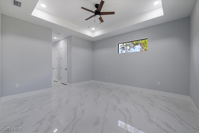 empty room featuring ceiling fan and a tray ceiling