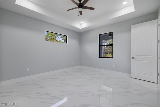 spare room with a raised ceiling, ceiling fan, and a healthy amount of sunlight