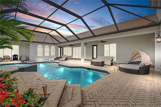 pool at dusk with a patio, ceiling fan, and glass enclosure