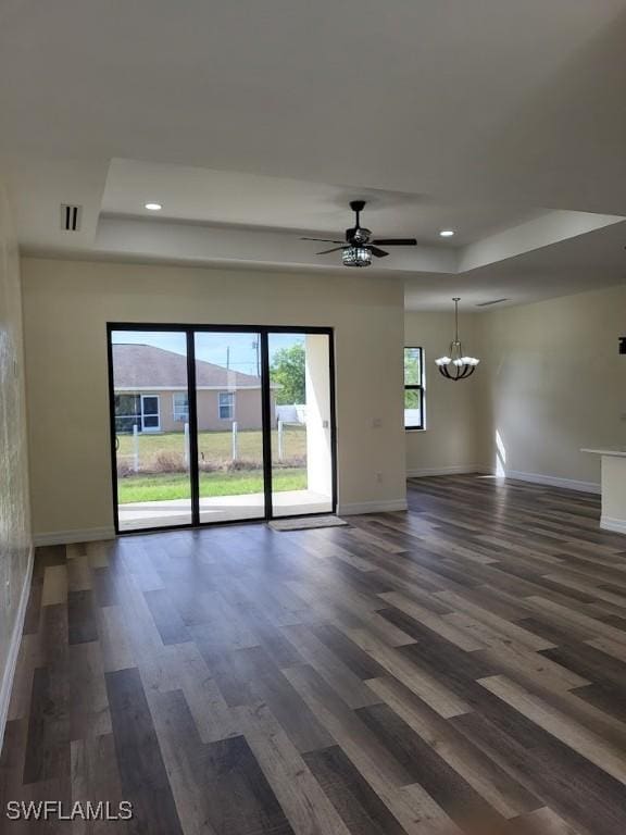 spare room featuring a tray ceiling, dark hardwood / wood-style flooring, and ceiling fan with notable chandelier