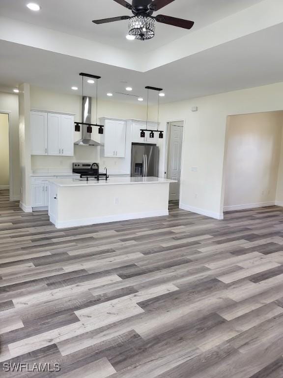 kitchen featuring pendant lighting, white cabinets, wall chimney range hood, an island with sink, and stainless steel appliances