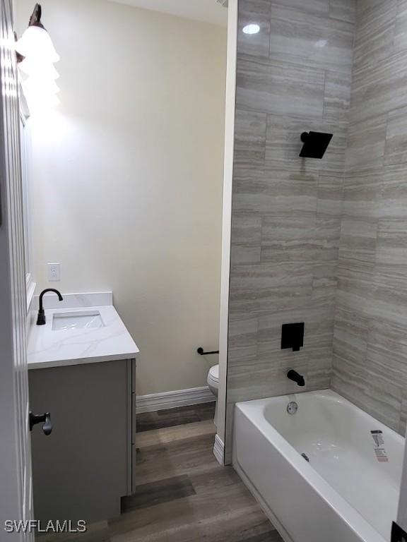 full bathroom with vanity, wood-type flooring, tiled shower / bath combo, and toilet