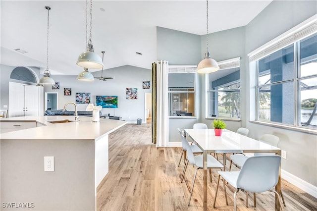 kitchen featuring white cabinets, sink, vaulted ceiling, light hardwood / wood-style flooring, and decorative light fixtures