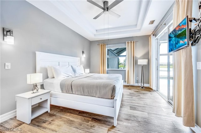 bedroom featuring access to outside, ceiling fan, light wood-type flooring, a tray ceiling, and multiple windows