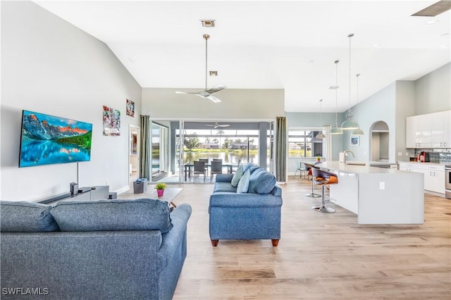 living room with ceiling fan, light hardwood / wood-style floors, sink, and high vaulted ceiling