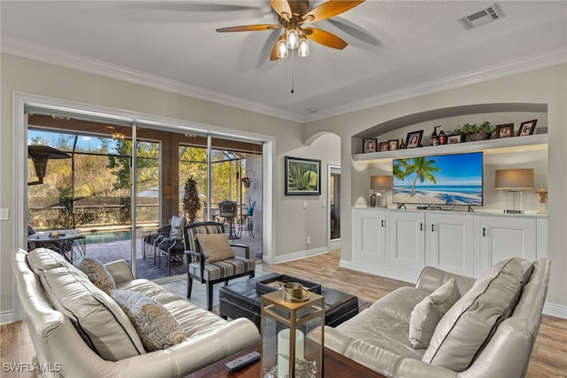 living room featuring built in shelves, ceiling fan, crown molding, and light wood-type flooring