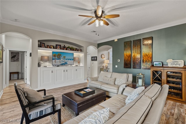 living room with built in shelves, light hardwood / wood-style flooring, ceiling fan, and ornamental molding