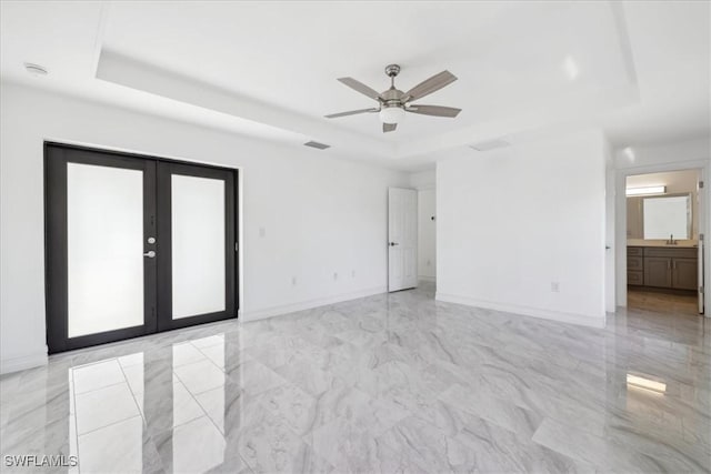 empty room featuring french doors, a tray ceiling, ceiling fan, and sink