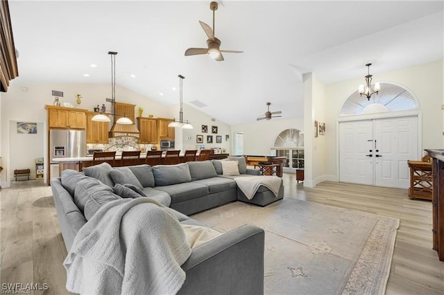 living room with ceiling fan with notable chandelier, high vaulted ceiling, and light hardwood / wood-style flooring