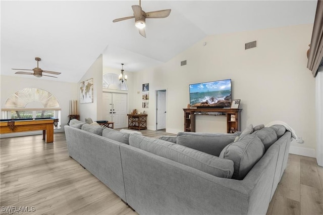 living room with ceiling fan with notable chandelier, high vaulted ceiling, and light hardwood / wood-style flooring