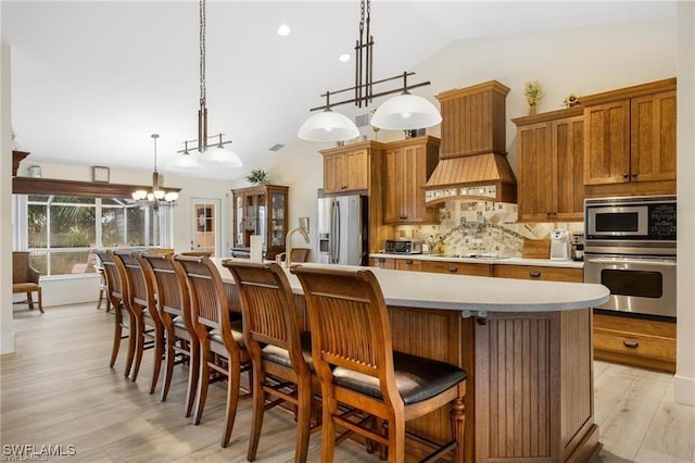 kitchen with decorative backsplash, appliances with stainless steel finishes, custom range hood, a large island with sink, and lofted ceiling