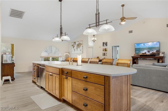 kitchen with light wood-type flooring, vaulted ceiling, sink, decorative light fixtures, and an island with sink