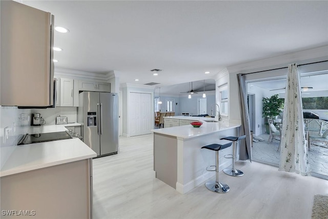 kitchen featuring sink, hanging light fixtures, stainless steel fridge, a kitchen bar, and kitchen peninsula