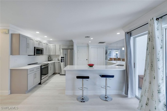 kitchen featuring sink, crown molding, a kitchen bar, gray cabinets, and appliances with stainless steel finishes