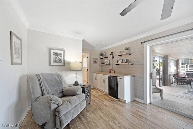 sitting room with crown molding, light hardwood / wood-style flooring, ceiling fan, and wood walls