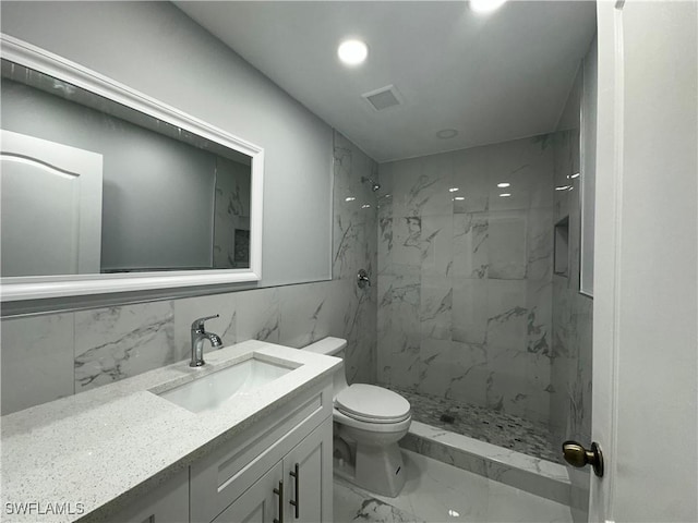 bathroom with a tile shower, vanity, tile walls, and toilet