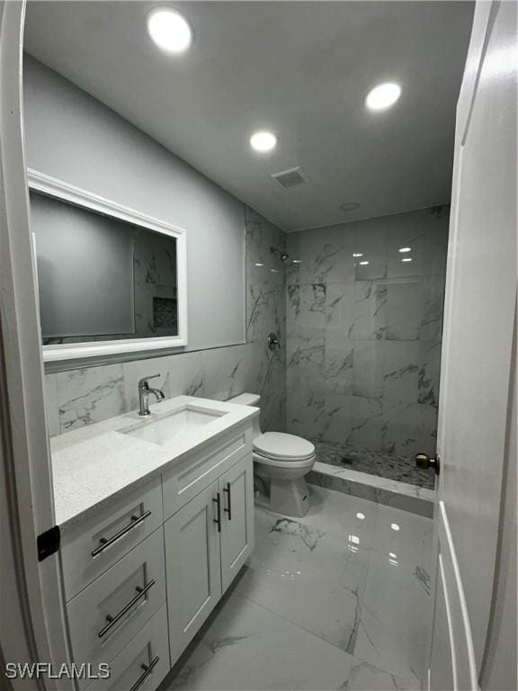 bathroom featuring a tile shower, vanity, and toilet