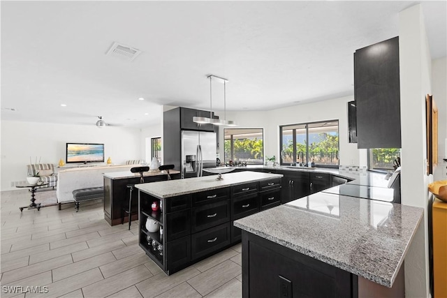 kitchen featuring light stone countertops, stainless steel fridge, sink, decorative light fixtures, and a kitchen island