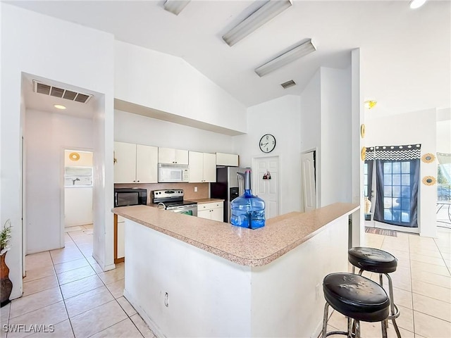 kitchen featuring stainless steel appliances, light tile patterned floors, lofted ceiling, a breakfast bar, and white cabinets