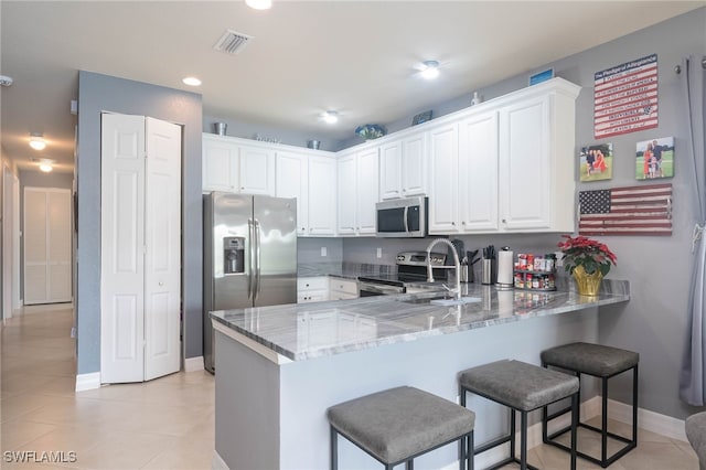 kitchen featuring appliances with stainless steel finishes, white cabinets, a kitchen bar, light stone counters, and kitchen peninsula