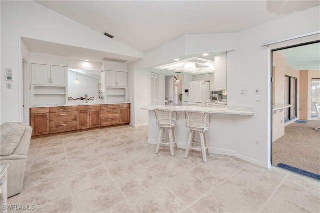 kitchen featuring lofted ceiling, a kitchen breakfast bar, kitchen peninsula, white fridge with ice dispenser, and white cabinetry