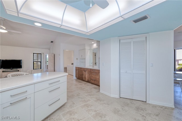 kitchen featuring ceiling fan, washer / dryer, white cabinetry, and vaulted ceiling