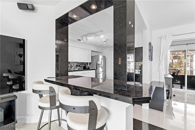 kitchen featuring a kitchen bar, stainless steel fridge, kitchen peninsula, tasteful backsplash, and white cabinets