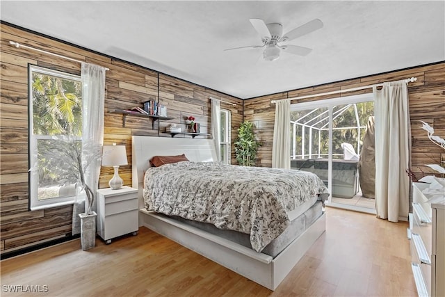 bedroom featuring access to outside, ceiling fan, light hardwood / wood-style floors, and wood walls