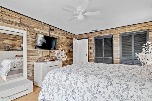 bedroom featuring light wood-type flooring, two closets, ceiling fan, and wood walls