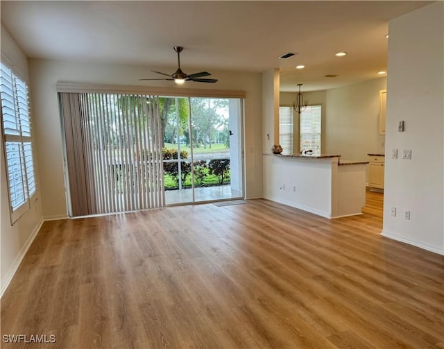 unfurnished living room featuring ceiling fan with notable chandelier and light hardwood / wood-style flooring