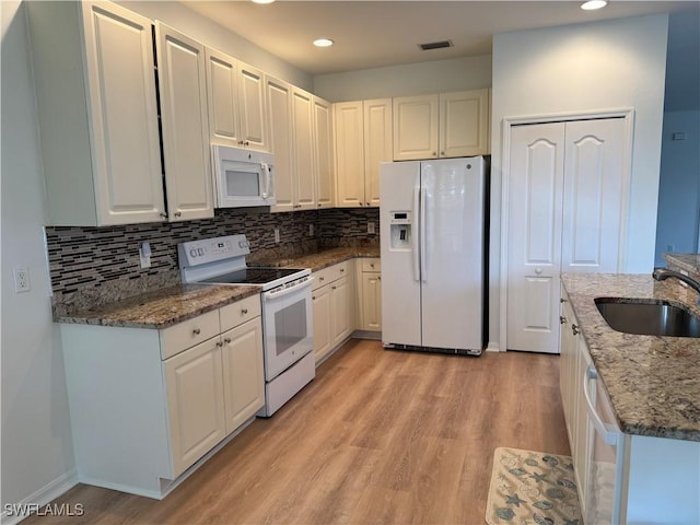 kitchen with dark stone countertops, white cabinetry, sink, and white appliances