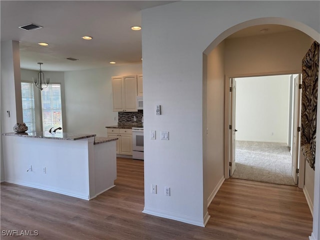 kitchen with backsplash, white appliances, light hardwood / wood-style flooring, a chandelier, and white cabinetry