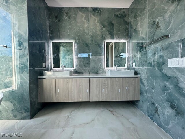 bathroom with double vanity, marble finish floor, tile walls, and a sink