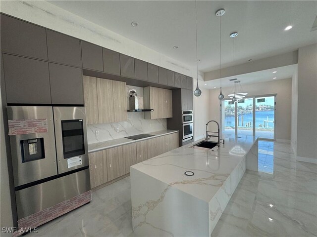 kitchen featuring sink, appliances with stainless steel finishes, hanging light fixtures, light stone counters, and a center island with sink