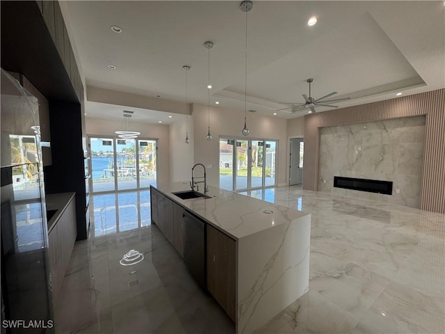 kitchen with a fireplace, sink, a large island with sink, ceiling fan, and a raised ceiling