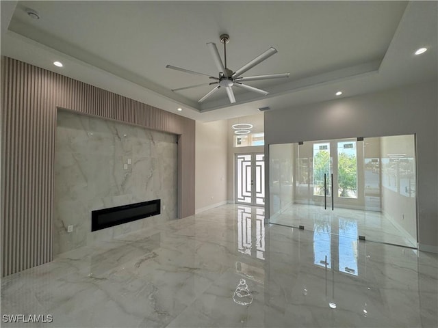 unfurnished living room with french doors, ceiling fan, a high end fireplace, and a tray ceiling