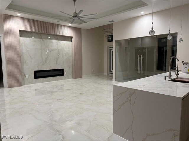 kitchen with pendant lighting, ceiling fan, sink, and light stone counters