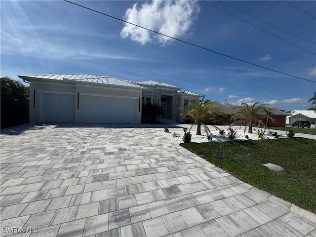 view of front of home with decorative driveway, an attached garage, a standing seam roof, metal roof, and a front lawn