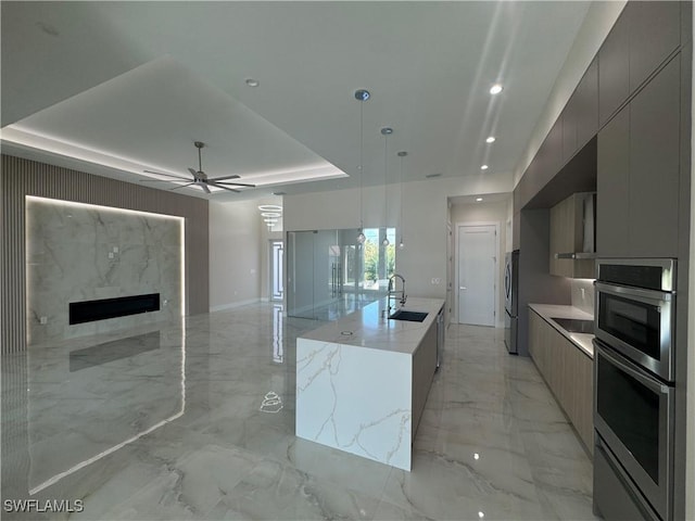 kitchen featuring a sink, open floor plan, marble finish floor, a tray ceiling, and modern cabinets