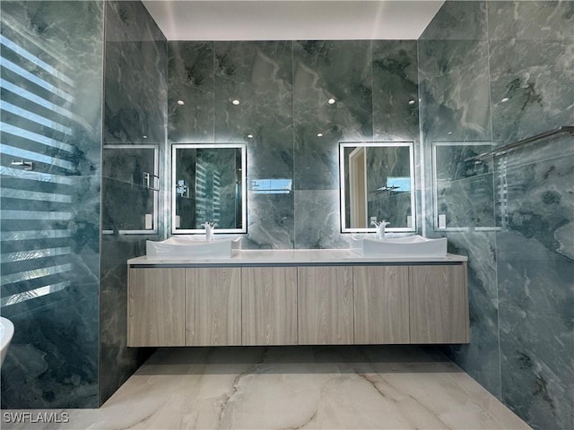 full bathroom with marble finish floor, a sink, tile walls, and double vanity