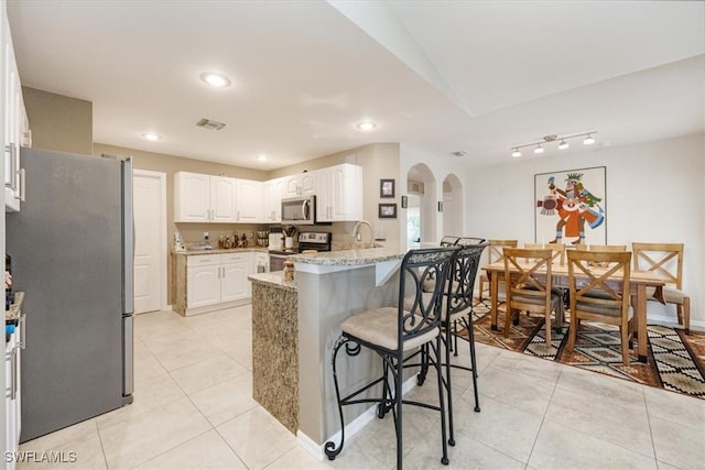 kitchen with a kitchen breakfast bar, light stone counters, stainless steel appliances, a center island with sink, and white cabinets