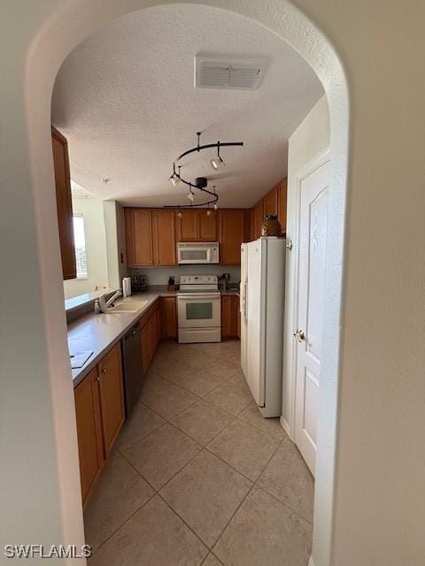 kitchen with track lighting, white appliances, a textured ceiling, sink, and light tile patterned floors