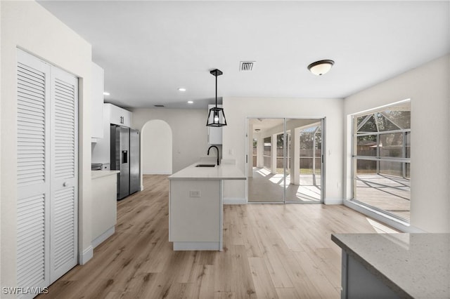 kitchen featuring pendant lighting, sink, stainless steel refrigerator with ice dispenser, light hardwood / wood-style flooring, and white cabinetry