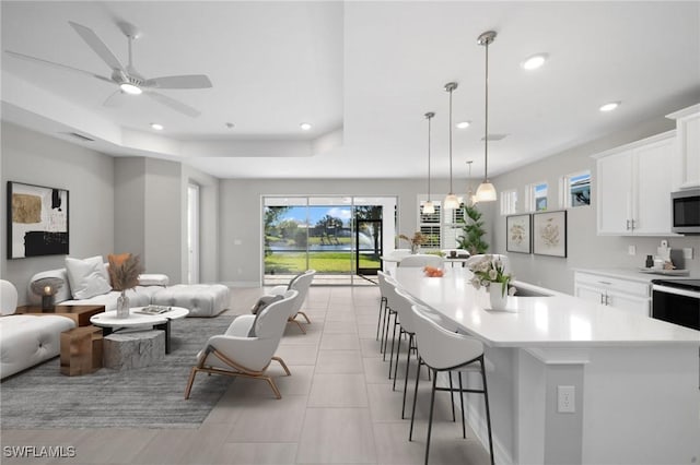 kitchen featuring a breakfast bar area, pendant lighting, white cabinets, and an island with sink