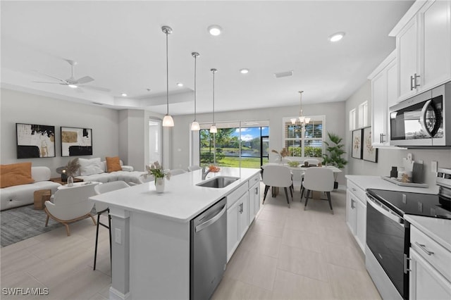 kitchen featuring white cabinetry, decorative light fixtures, an island with sink, stainless steel appliances, and ceiling fan with notable chandelier