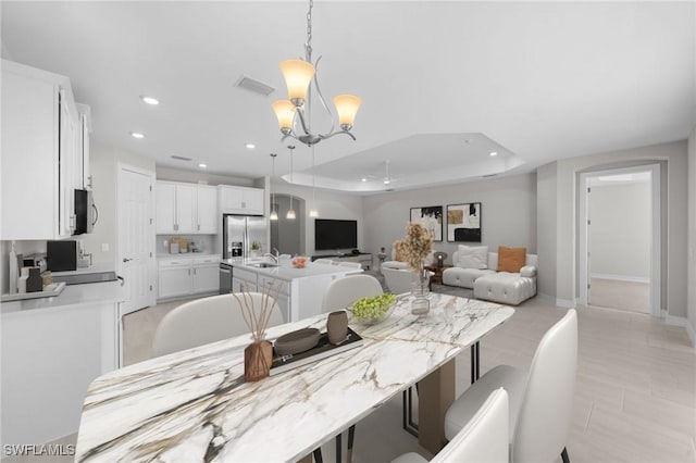 dining area with a raised ceiling, sink, and an inviting chandelier