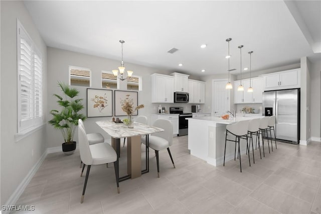 kitchen with white cabinets, hanging light fixtures, stainless steel appliances, and a kitchen island with sink