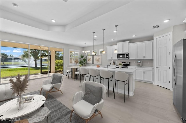 kitchen with an island with sink, a wealth of natural light, decorative light fixtures, white cabinetry, and stainless steel appliances